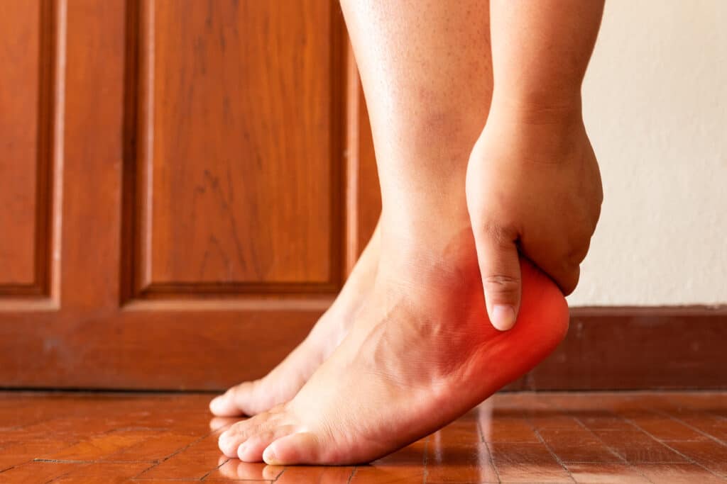 person holding the back of their foot, which is highlighted red at the heel to show pain